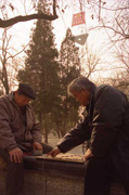 2 chiniese play chinese chess in the park , in the background you can see the old television tower with the laowai banner